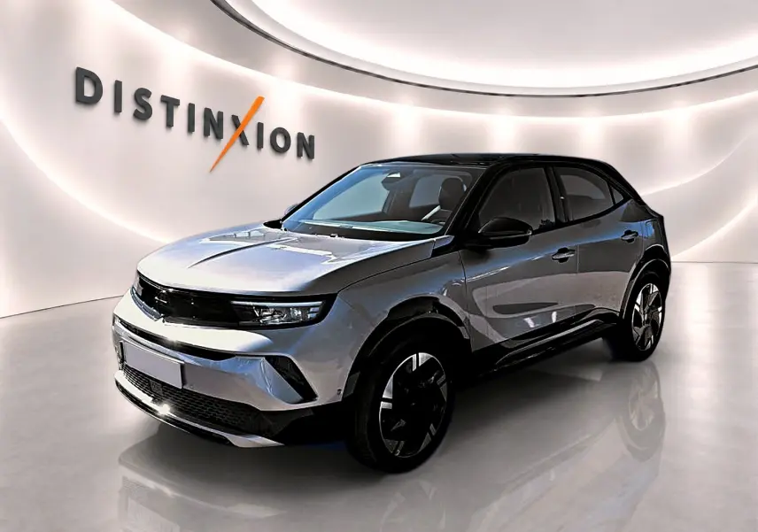 Opel Mokka Electric gris en 3/4 avant droit, avec toit noir et jantes alu distinctives dans un showroom lumineux.