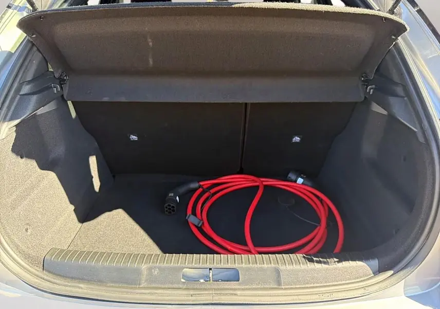 Coffre ouvert d’un Opel Mokka Electric gris 2025 avec câble de recharge électrique rouge enroulé.