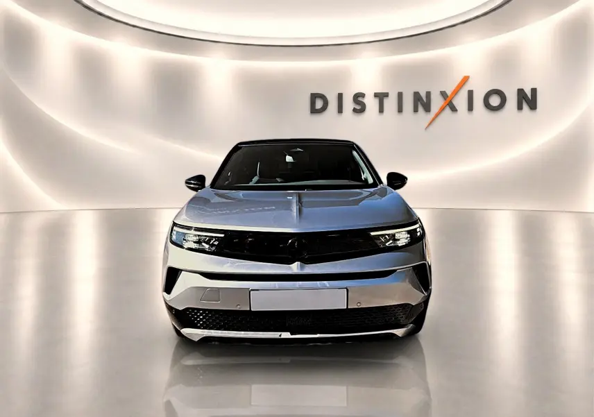 Vue frontale d'un Opel Mokka Electric gris 2025, avec calandre noire et éclairage LED, sur fond lumineux "Distinxion".