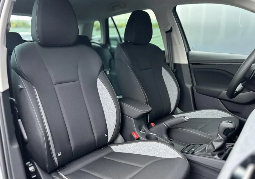 Vue intérieure sur les sièges avant en tissu noir et gris clair du Skoda Kamiq TSI 116 DSG7, avec accoudoir central.