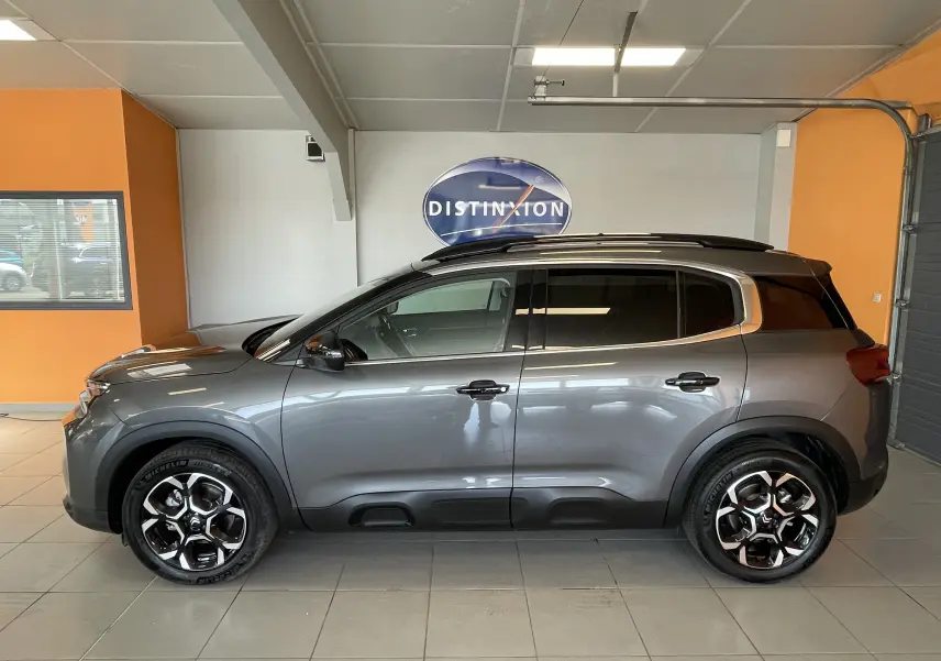 Vue de profil côté gauche du Citroën C5 Aircross hybride gris platinium avec jantes alliage 18 pouces biton en intérieur showroom.