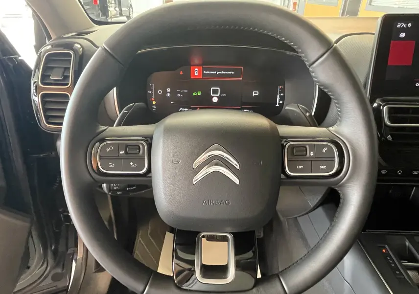 Vue rapprochée du volant en cuir noir du Citroën C5 Aircross gris platinium, avec tableau de bord digital et commandes intégrées.