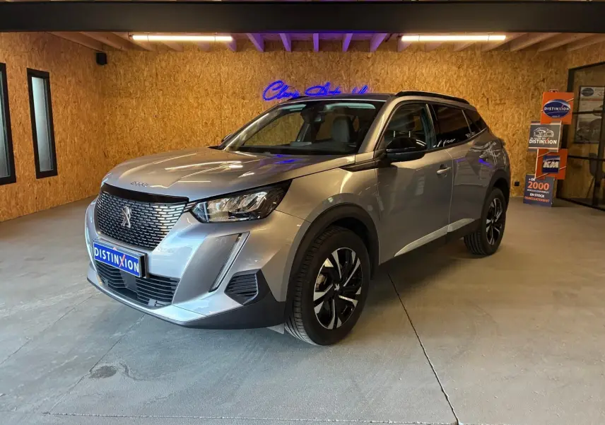 Peugeot 2008 gris métallisé vue 3/4 avant droit dans un showroom avec jantes noires et toit noir.