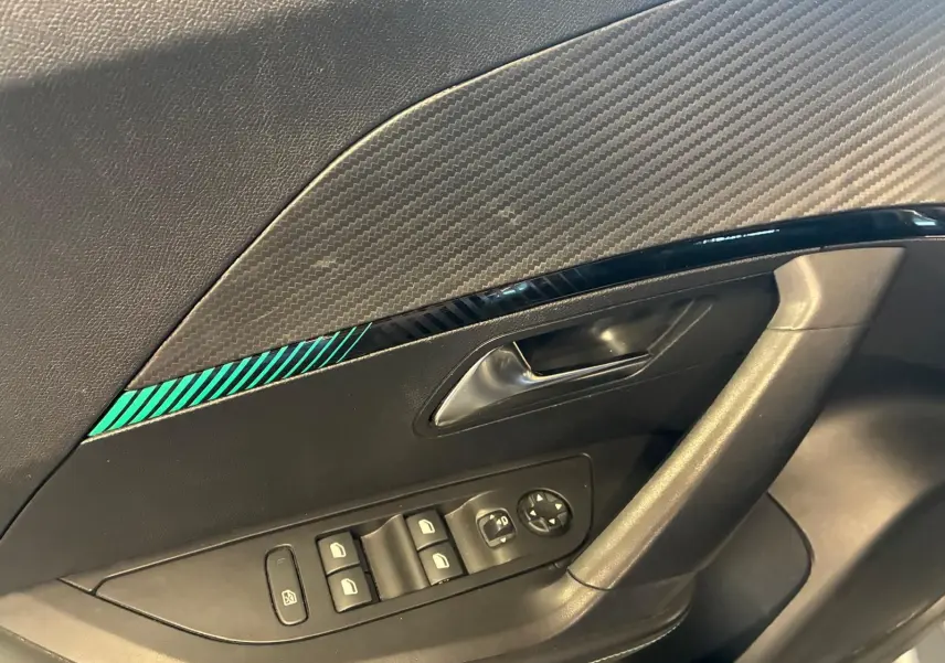 Détail de la porte côté conducteur du Peugeot 2008 gris, avec commandes de vitres et insert décoratif noir à rayures vertes.