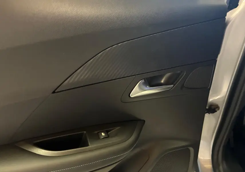 Détail de la porte intérieure côté gauche du Peugeot 2008 gris, avec poignée argentée et insert effet carbone.