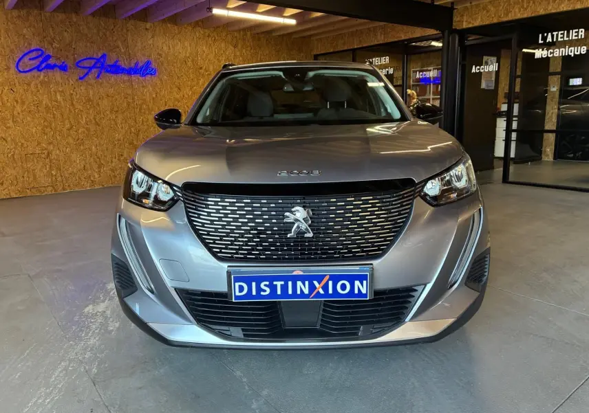 Vue avant d'un Peugeot 2008 gris 2022 avec calandre noire et phares LED allumés en intérieur showroom.