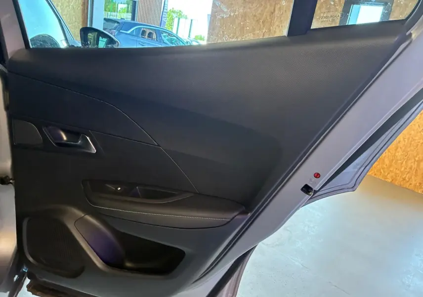 Vue intérieure de la porte arrière gauche noire du Peugeot 2008 gris 2022, mettant en valeur la poignée et les commandes.