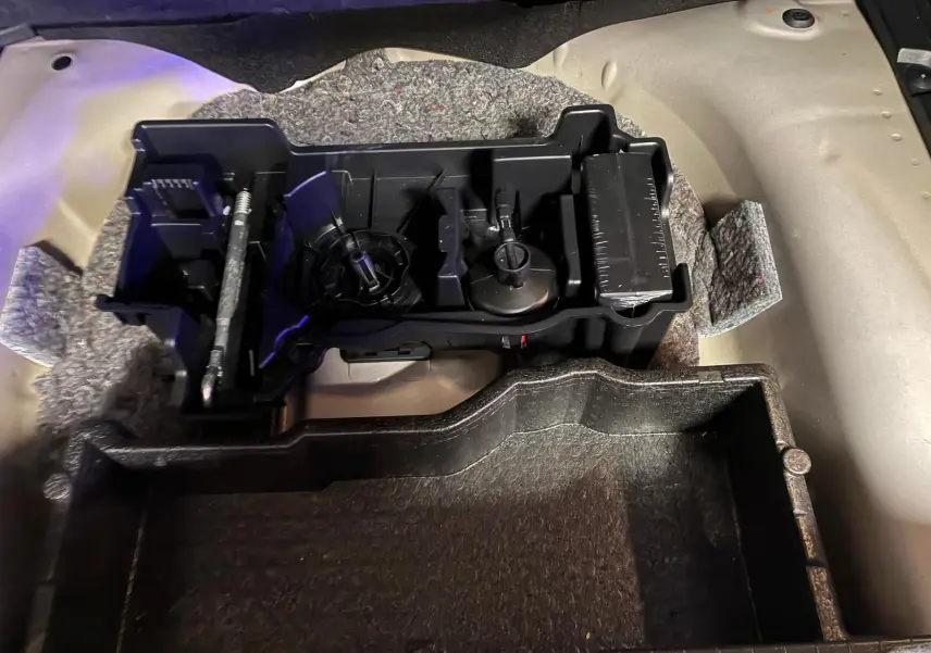 Vue rapprochée du rangement sous le plancher du coffre d'un Peugeot 2008 gris, montrant les compartiments en plastique.