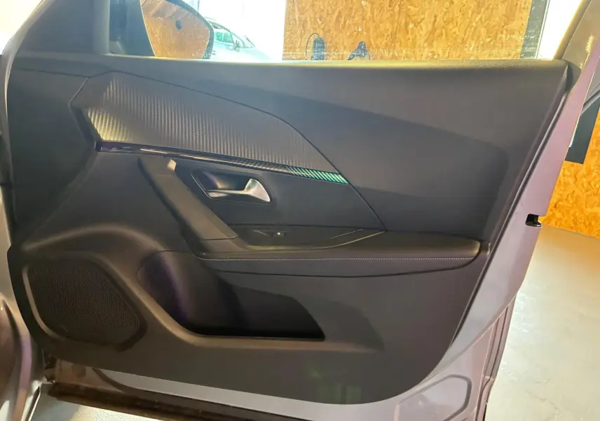Vue intérieure de la porte avant gauche d’un Peugeot 2008 gris, avec habillage noir et insert décoratif texturé.