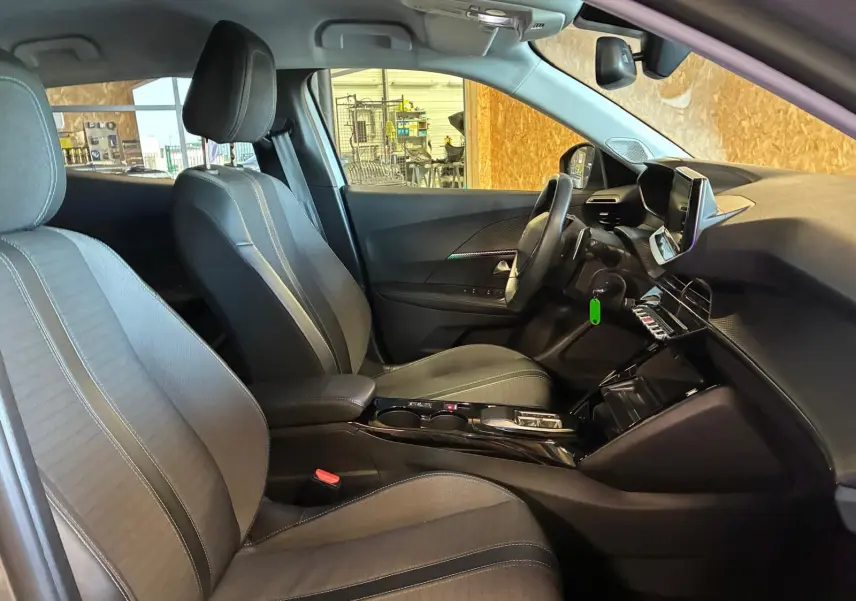 Vue intérieure côté gauche du poste de conduite du Peugeot 2008 gris, mettant en valeur les sièges tissu noirs et la console centrale moderne.