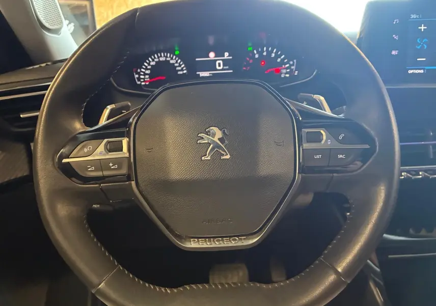 Vue rapprochée du volant noir du Peugeot 2008 1.5 BlueHDi 130 avec commandes intégrées et tableau de bord numérique.