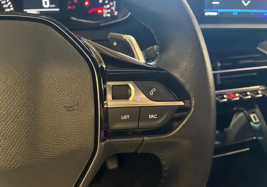 Gros plan sur la partie gauche du volant en cuir noir du Peugeot 2008, avec commandes audio et tableau de bord en arrière-plan.