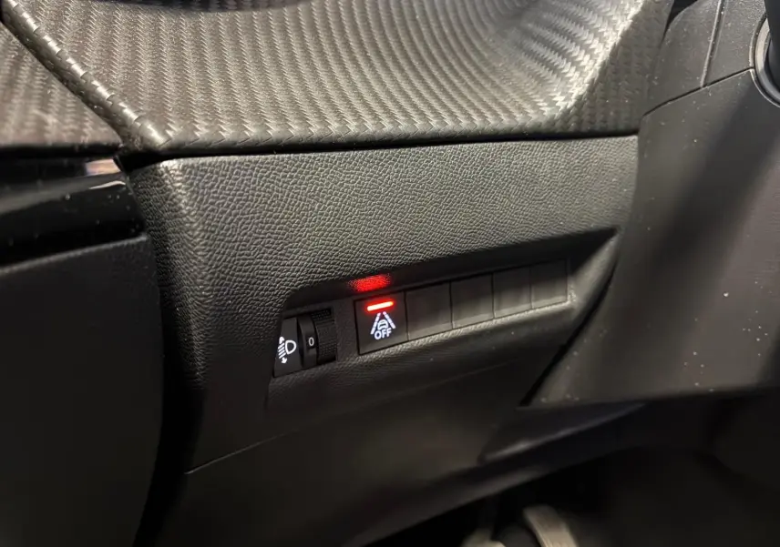 Gros plan sur les commandes noires du tableau de bord côté conducteur du Peugeot 2008 gris, avec témoin lumineux rouge actif.