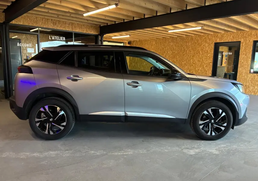 Peugeot 2008 gris vue de profil côté gauche, avec jantes noires et toit noir dans un garage.