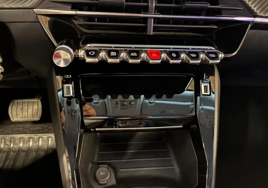 Vue rapprochée de la console centrale noire brillante du Peugeot 2008 1.5 BlueHDi 130, avec boutons de commande alignés.