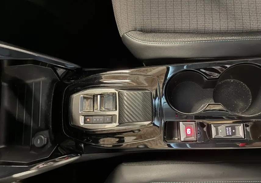 Vue plongeante sur la console centrale noire brillante du Peugeot 2008 gris, avec levier de vitesses électronique et porte-gobelets.