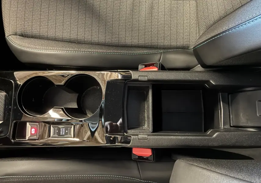 Vue plongeante sur la console centrale noire brillante du Peugeot 2008 1.5 BlueHDi 130, avec porte-gobelets et rangement ouvert.