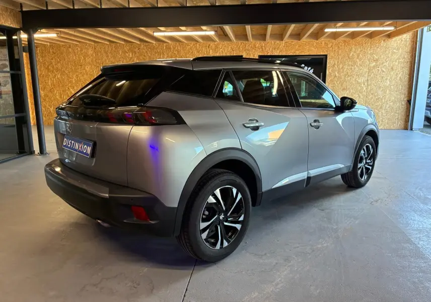 Peugeot 2008 gris métallisé vue 3/4 arrière droit dans un showroom avec toit noir et jantes alliage bicolores.