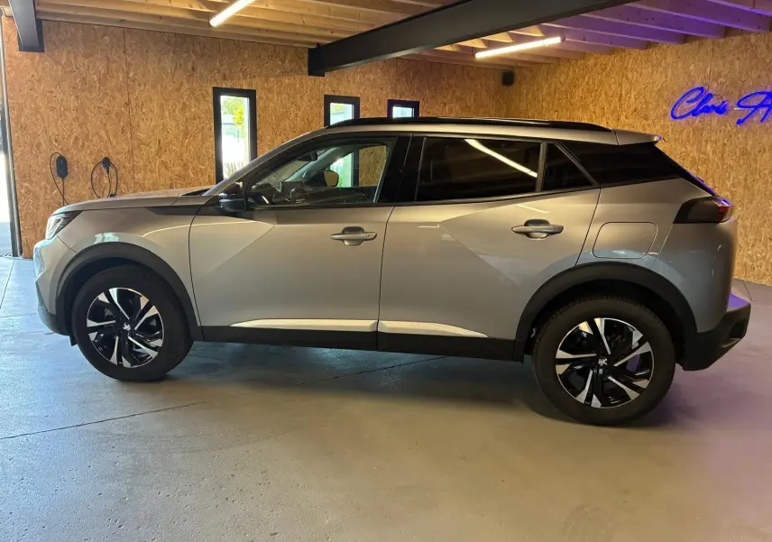 Profil droit d’un Peugeot 2008 gris 2022 avec toit noir et jantes alliage bicolores, stationné en intérieur.