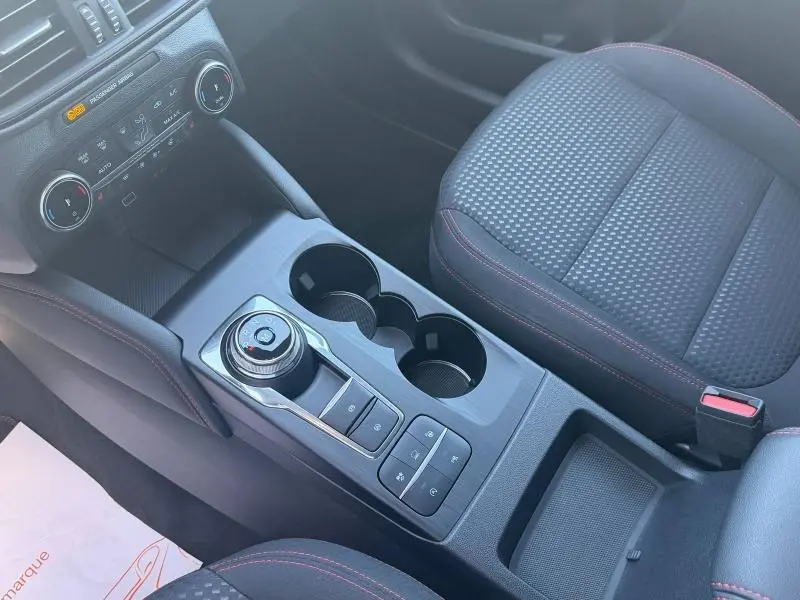 Vue rapprochée de la console centrale du Ford Kuga 2024, avec sélecteur rotatif de boîte auto et sièges tissu noir à surpiqûres rouges.