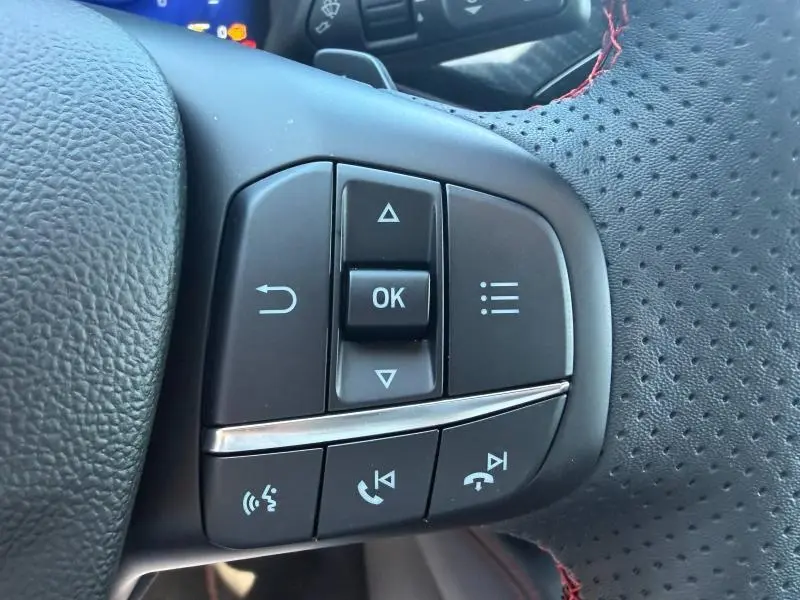 Gros plan sur les commandes multifonctions à droite du volant cuir perforé avec surpiqûres rouges du Ford Kuga gris Solar 2024.