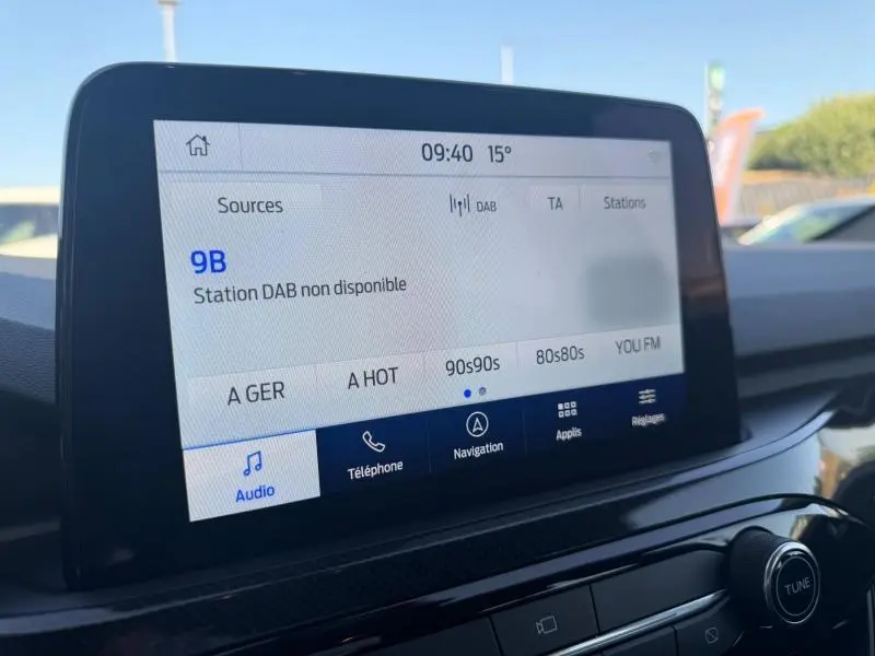 Écran tactile central de la Ford Kuga 2024 affichant la radio DAB, vue intérieure avant, tableau de bord noir.