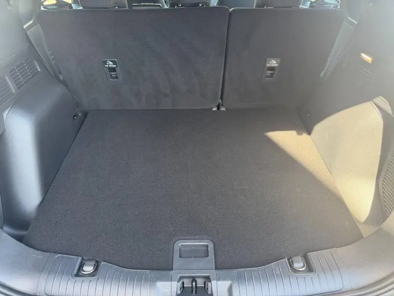 Vue du coffre spacieux et propre du Ford Kuga 2024, avec banquette arrière noire rabattue et moquette sombre.