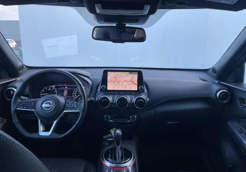 Vue intérieure avant du Nissan Juke 2024 avec tableau de bord noir, écran tactile central et volant cuir.