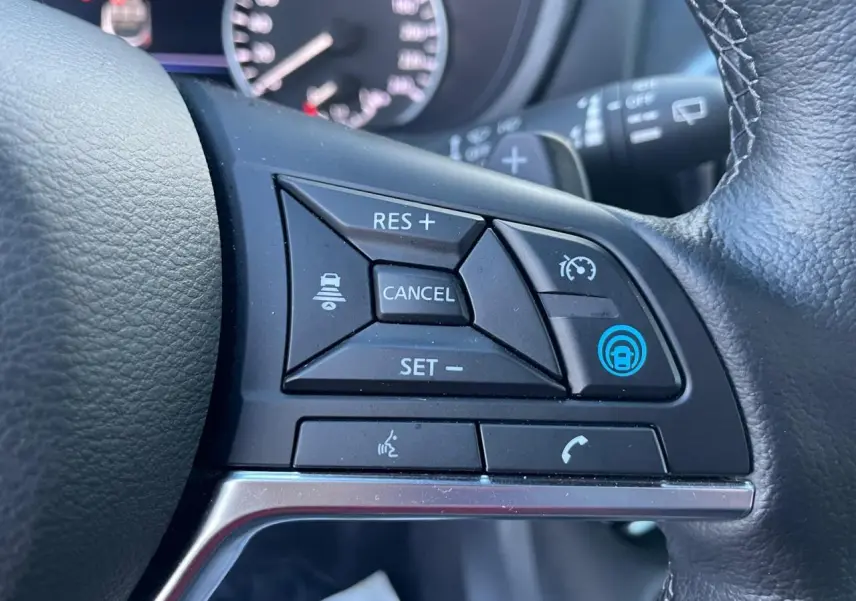 Gros plan sur les commandes de régulateur adaptatif au volant cuir du Nissan Juke II bleu Magnetic 2024