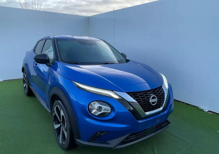 Nissan Juke II bleu magnetic en 3/4 avant droit, avec calandre V-motion chromée et jantes alliage noires.