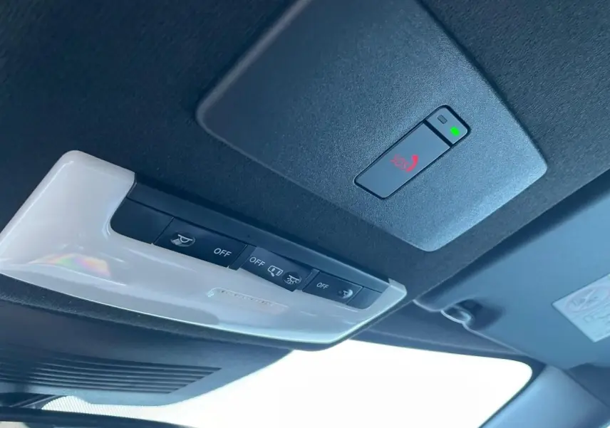 Gros plan sur la console de toit noire avec bouton SOS rouge et éclairage intérieur blanc du Nissan Juke II bleu magnetic 2024.