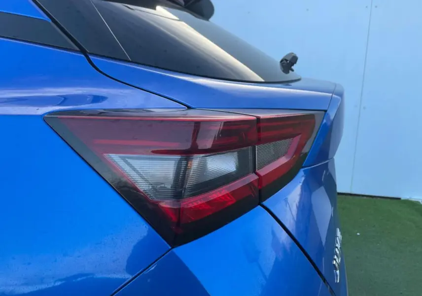 Gros plan sur le feu arrière droit bleu magnetic du Nissan Juke II 2024 avec antenne aileron de requin noire.