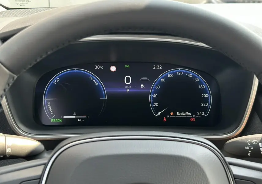 Tableau de bord numérique vu de face dans une Toyota Corolla Touring Sport 1.8 Hybrid 140 Sport blanc, affichage vitesse et énergie hybride.