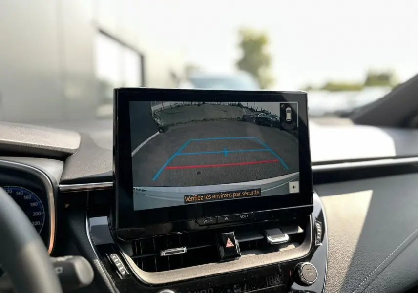 Écran central montrant la caméra de recul d'une Toyota Corolla Touring Sport blanche, vue intérieure avant.