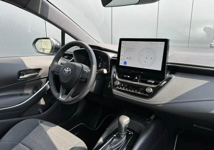 Vue intérieure côté conducteur de la Toyota Corolla Touring Sport 2025, tableau de bord noir avec écran tactile et volant multifonction.