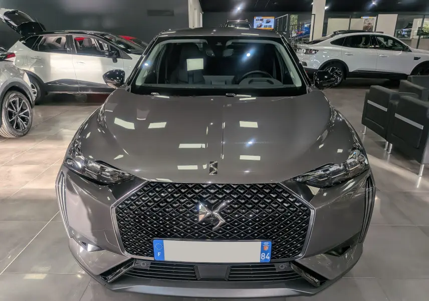 Vue avant d'une DS3 2024 gris Platinium avec calandre noire distinctive et phares LED en showroom.