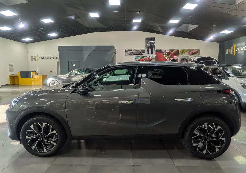 Vue de profil côté gauche d'une DS3 2024 gris Platinium avec jantes bi-ton noires dans un showroom.