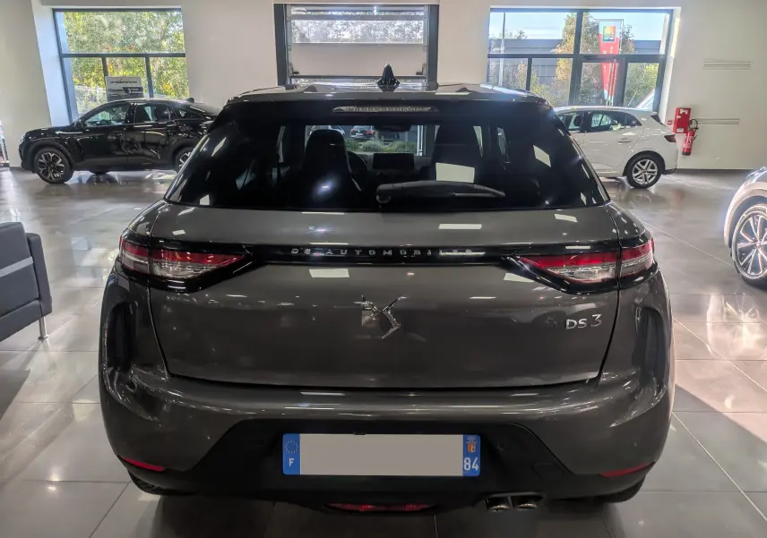 Vue arrière d'une DS3 gris Platinium 2024 dans un showroom, mettant en valeur ses feux LED et son logo DS Automobiles.