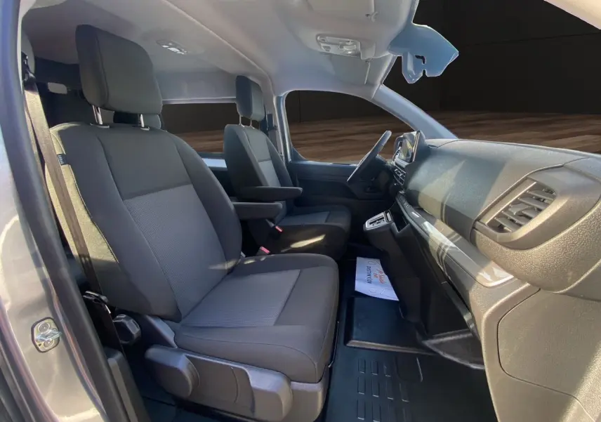 Intérieur avant du Citroën Jumpy XL gris acier, sièges tissu noir avec accoudoirs et tableau de bord moderne.