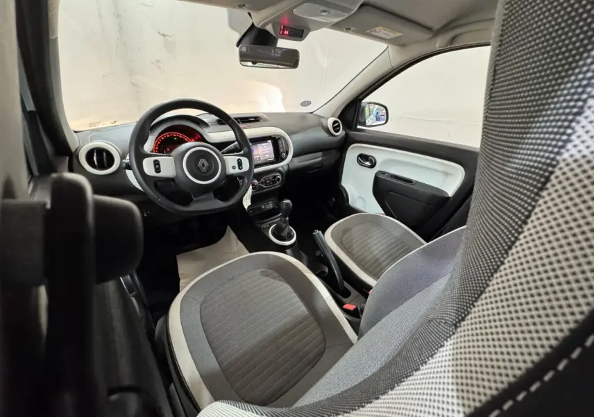 Intérieur Renault Twingo blanc vu côté conducteur, volant multifonctions, tableau de bord avec écran tactile et sièges gris.