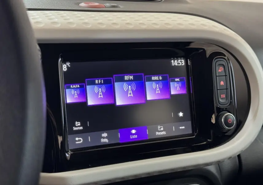 Écran tactile central de la Renault Twingo blanc 2022 affichant les stations radio avec commandes latérales.
