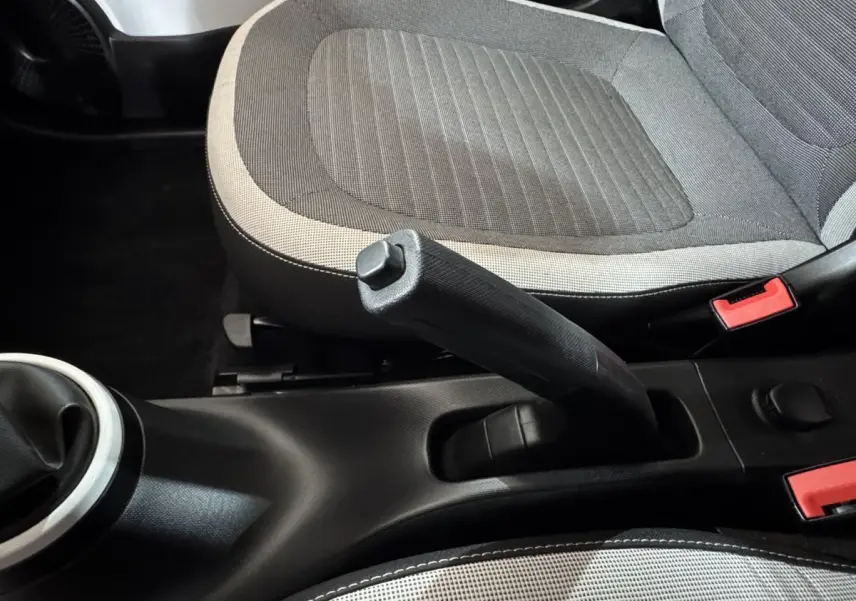 Vue rapprochée de la console centrale et frein à main entre les sièges gris clair et foncé d'une Renault Twingo blanche.