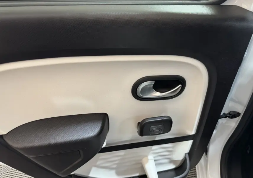 Gros plan sur la porte intérieure côté gauche de la Renault Twingo blanche, montrant la poignée et le bouton d'ouverture du coffre.