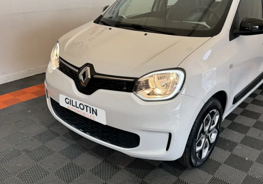 Vue 3/4 avant droite d'une Renault Twingo blanche 2022 avec phares allumés et jantes distinctives.