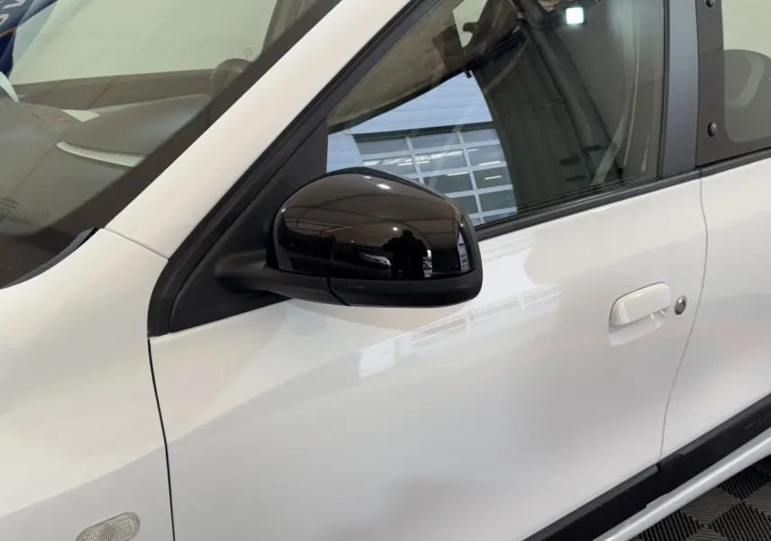 Zoom sur la portière côté gauche d'une Renault Twingo blanche avec rétroviseur noir brillant et poignée intégrée.