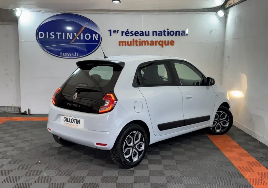 Renault Twingo Equilibre blanc vue 3/4 arrière droit en intérieur avec jantes distinctives et vitres teintées.