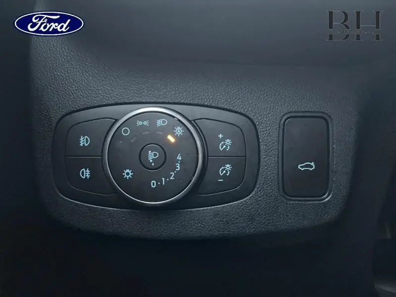 Vue rapprochée du panneau de commande des phares et du bouton d'ouverture du hayon du Ford Puma blanc Glacier 2020.