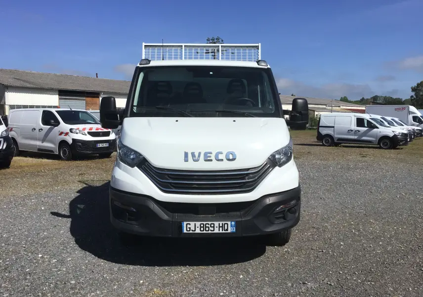 Vue avant d'un Iveco Daily Chassis Cabine blanc avec benne acier et coffre, stationné sur un terrain gravillonné.