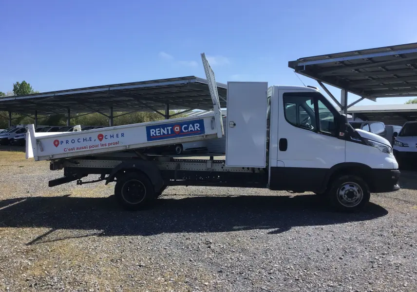 Vue latérale droite d'un Iveco Daily blanc avec benne basculante et coffre latéral, marquage Rent a Car visible.