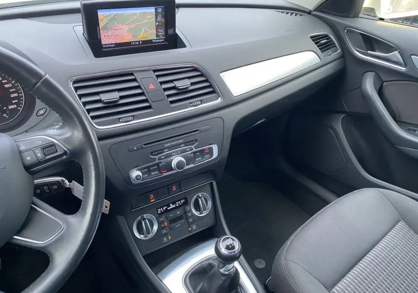 Vue intérieure côté passager avant de l'Audi Q3 2.0 TDI blanc, avec GPS intégré et boîte manuelle visible.